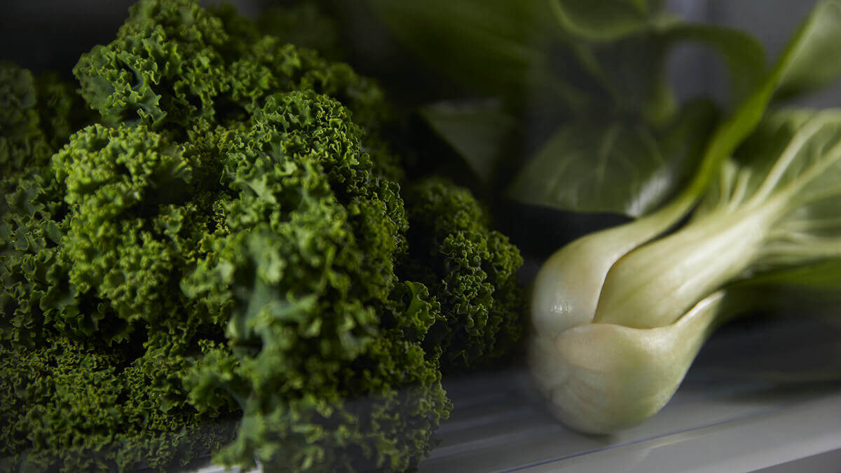 Close-up of fresh kale and bok choy in a humidity-controlled refrigerator drawer